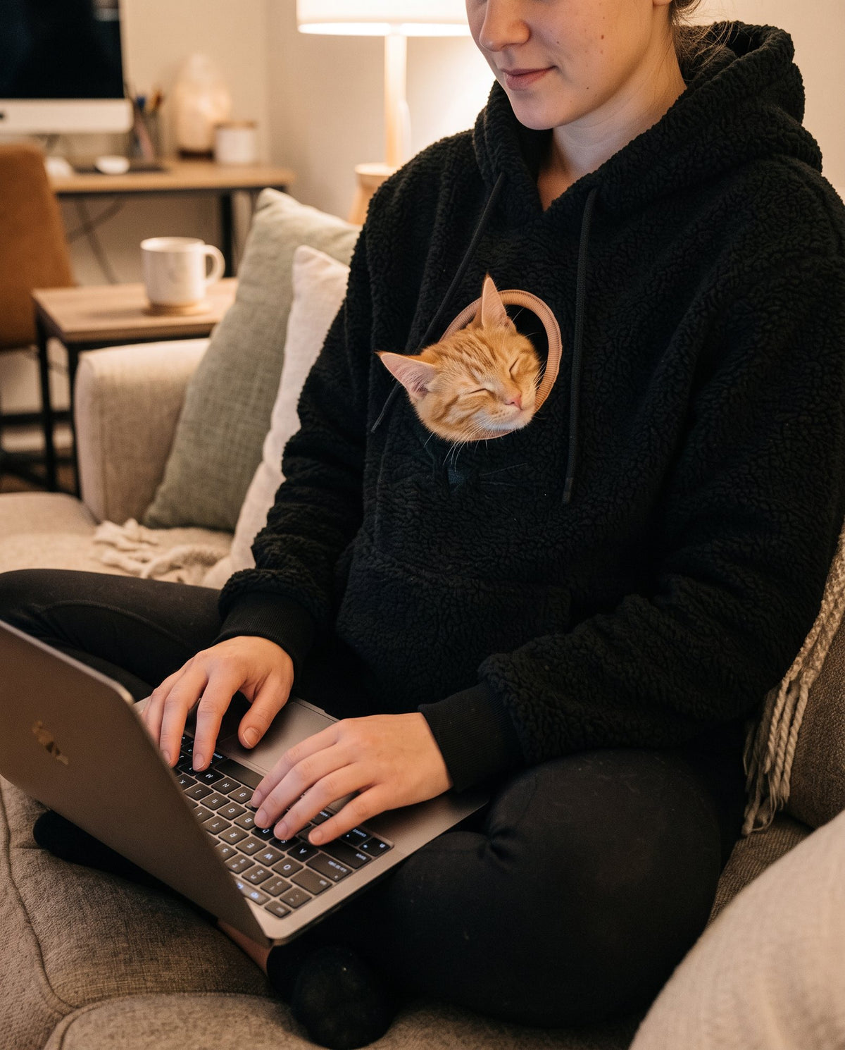 Woman working on a laptop with a cat asleep in her hoodie